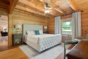 Ein Schlafzimmer einer Holzhütte mit Bett, Nachttischen, Schreibtisch und einem Fenster mit Vorhängen.
