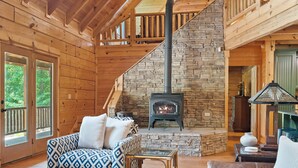 A log cabin interior with a stone fireplace, wooden walls, and a staircase.