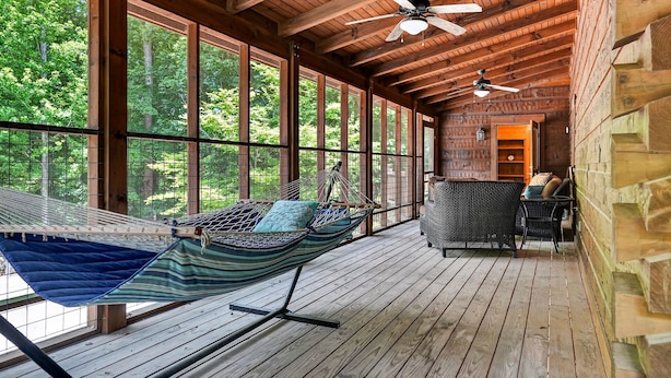 A wooden deck with a hammock, wicker furniture, and a ceiling fan.
