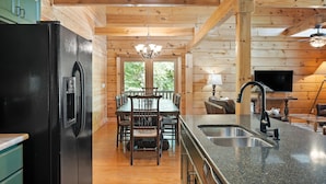 A wooden interior with a black refrigerator, dining table, chairs, and a kitchen counter with a sink.