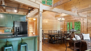 A wooden cabin interior with a kitchen, dining area, and a cozy seating area.