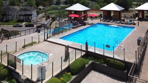 A swimming pool with a hot tub, lounge chairs, and umbrellas.