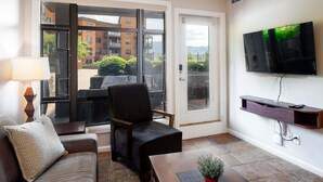 A living room with a sofa, a chair, a TV mounted on the wall, and a door leading to an outdoor area.
