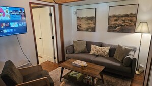 Ein Wohnzimmer mit einer Couch, einem Sessel, einem Couchtisch und einem an der Wand befestigten Fernseher.