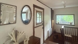Ein Zimmer mit einem hölzernen Schminktisch, einem Spiegel, einem gerahmten Bild und einem Fenster mit Blick auf Grünflächen.