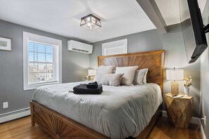 Una camera da letto con un letto in legno, pareti grigie, una lampada a soffitto e una TV a muro.