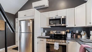 A modern kitchen with stainless steel appliances, white cabinetry, and a black countertop.