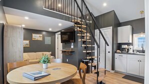 A modern kitchen with white cabinets, a wooden staircase, and a dining area with a round table and chairs.