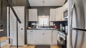 A modern kitchen with white cabinets, a stainless steel refrigerator, a built-in oven, and a black countertop.