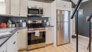 A modern kitchen with white cabinets, a stainless steel refrigerator, a microwave, and an oven.
