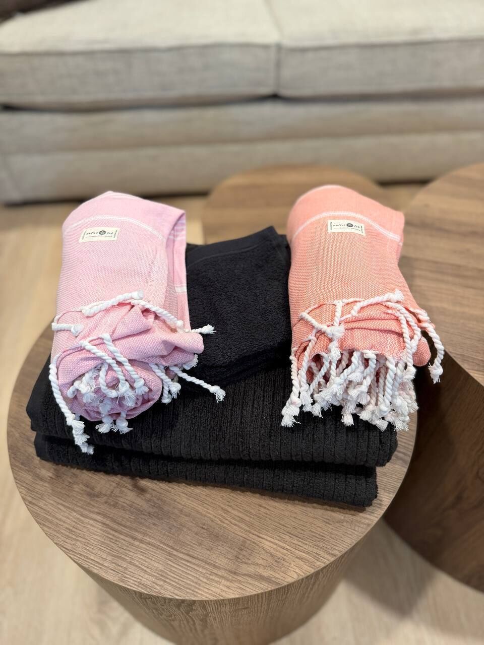 A pair of pink towels with white tassels on a wooden surface.