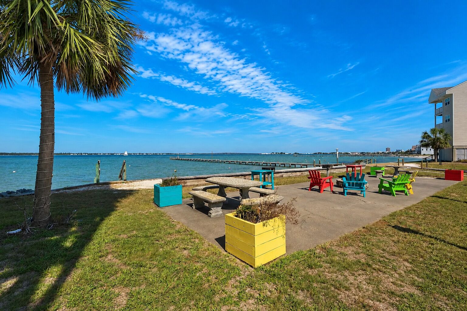 A waterfront patio with outdoor seating, a palm tree, and a view of the water.