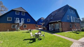 Ein Wohnhaus mit einem großen blauen Gebäude, einem kleineren Anbau und einem gepflegten Rasen mit Außenmöbeln.