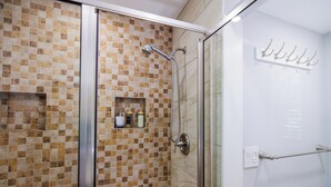 Una cabina doccia con porta in vetro, parete rivestita di piastrelle e porta asciugamani.