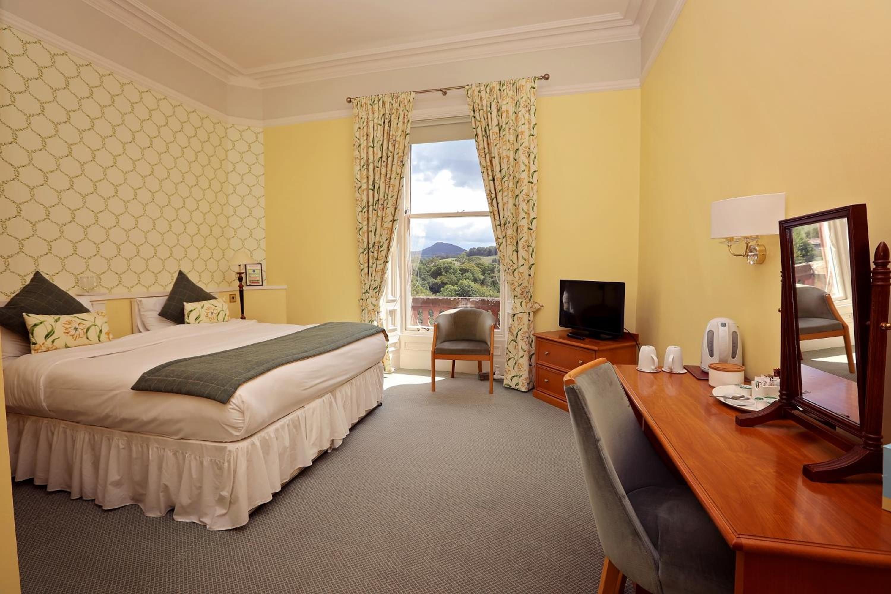 A hotel room with a bed, a desk, a chair, a television, and a view of the outdoors.