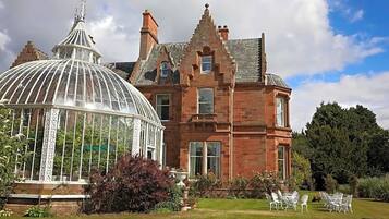 A large red brick building with a glass conservatory and a well-maintained garden.