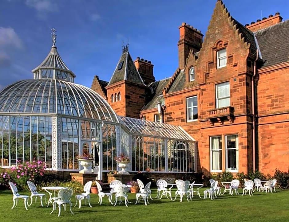 A historic building with a glass conservatory, white chairs, and a well-maintained lawn.
