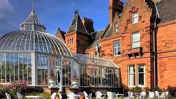 A historic building with a glass conservatory, white chairs, and a well-maintained lawn.