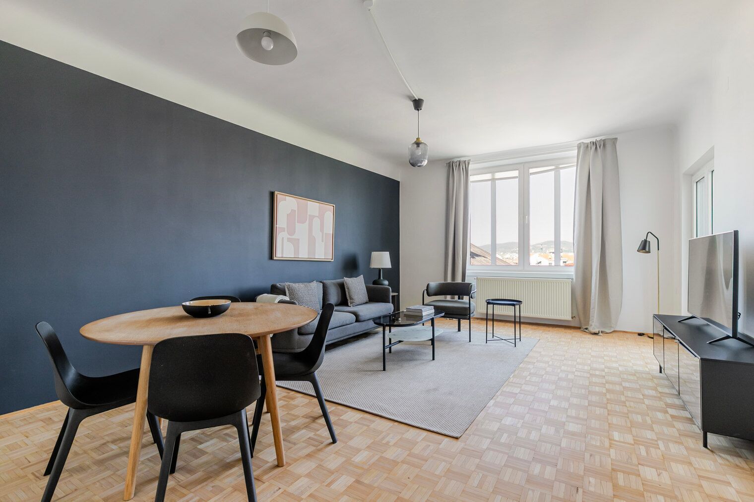A modern living room with a dining area, a sofa, a TV, and a large window.