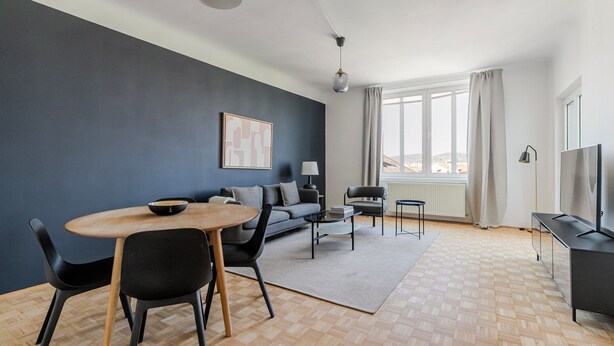 Ett modernt vardagsrum med en matplats, en soffa, en tv och ett stort fönster.