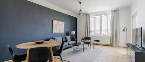 A modern living room with a dining area, a sofa, a TV, and a large window.