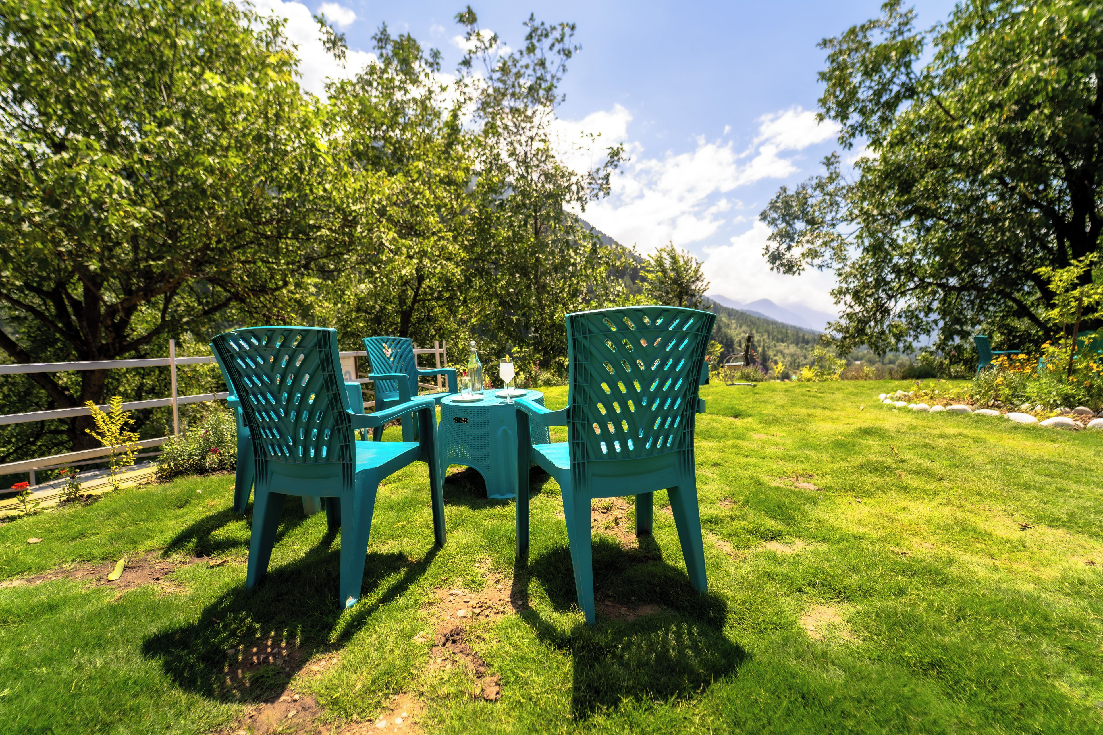 A grassy outdoor area with a table and chairs, surrounded by trees and a fence.