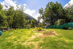 A well-maintained grassy area with a circular flower bed, surrounded by trees and a mountain backdrop. - Hotel Gulsar pahalgam  (Pahalgam)