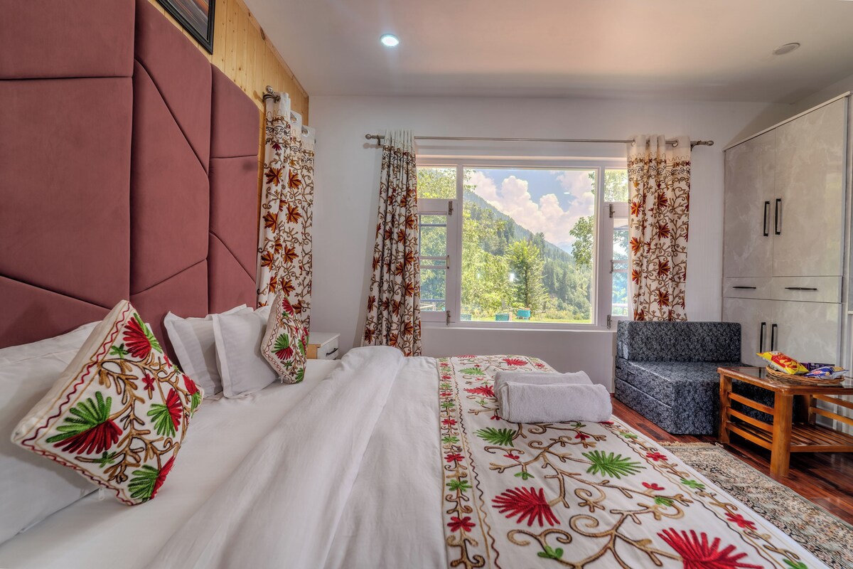 A bedroom with a large bed, a chair, a wardrobe, and a window with a view of trees.