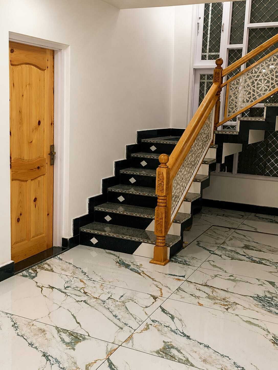 A staircase with black steps and a wooden handrail, leading to a room with a white door and a window with a decorative grille.