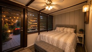A bedroom with a bed, a nightstand, a ceiling fan, and a view through a glass door to an outdoor area with a fire. - River Ranch Luxury Retreat | Cozy 1BR Cabin 303 (River Ranch)