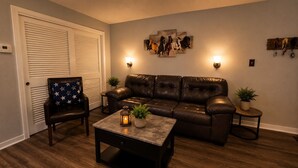 A living room with a leather sofa, a coffee table, a chair with a star-patterned pillow, wall-mounted lights, and a horse-themed artwork. - River Ranch Luxury Retreat | Cozy 1BR Cabin 303 (River Ranch)