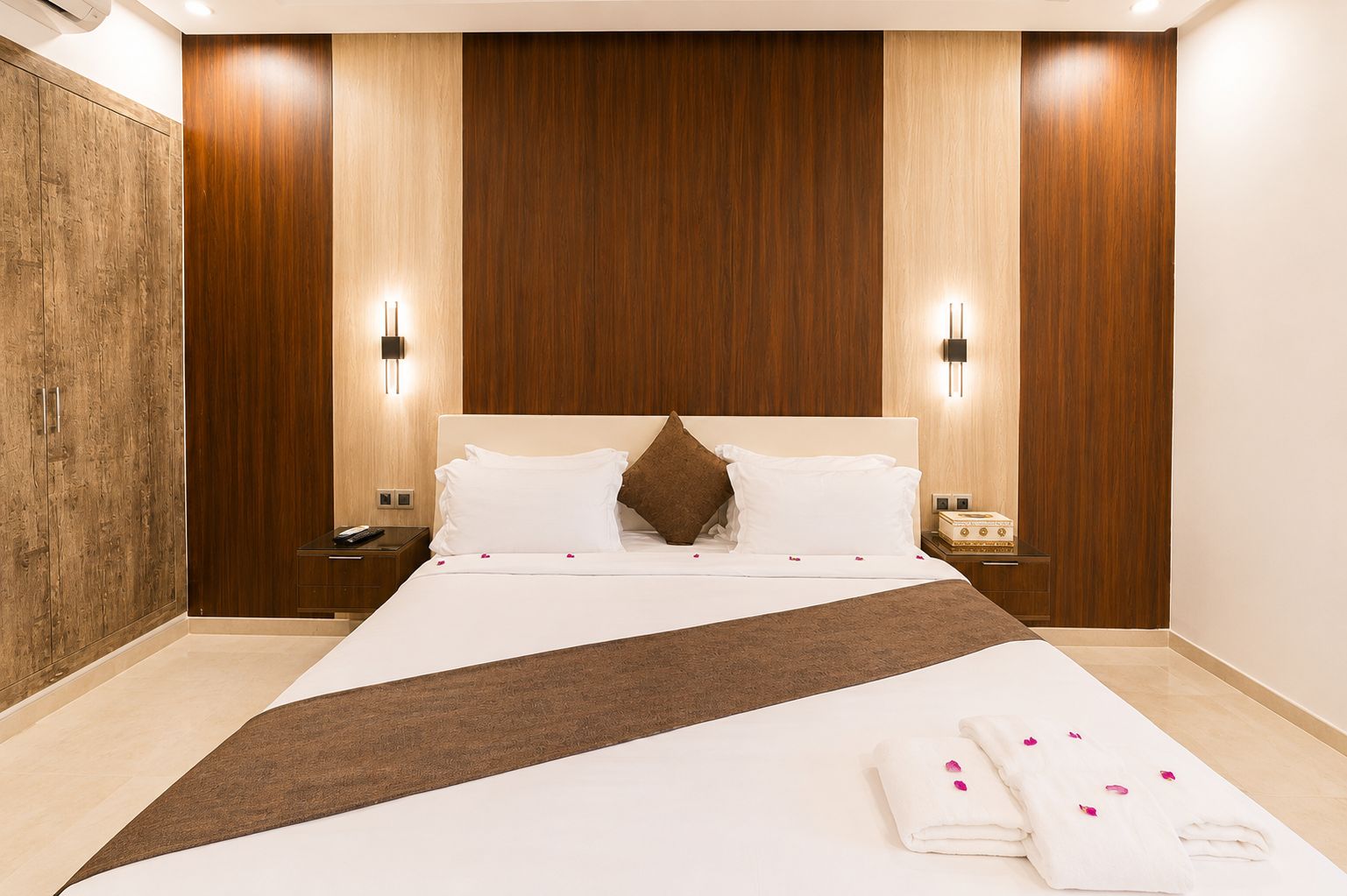 Ein Hotelzimmer mit einem großen Bett, Holzwandverkleidung, zwei Nachttischen mit Lampen und einem Beistelltisch ebenfalls mit einer Lampe.