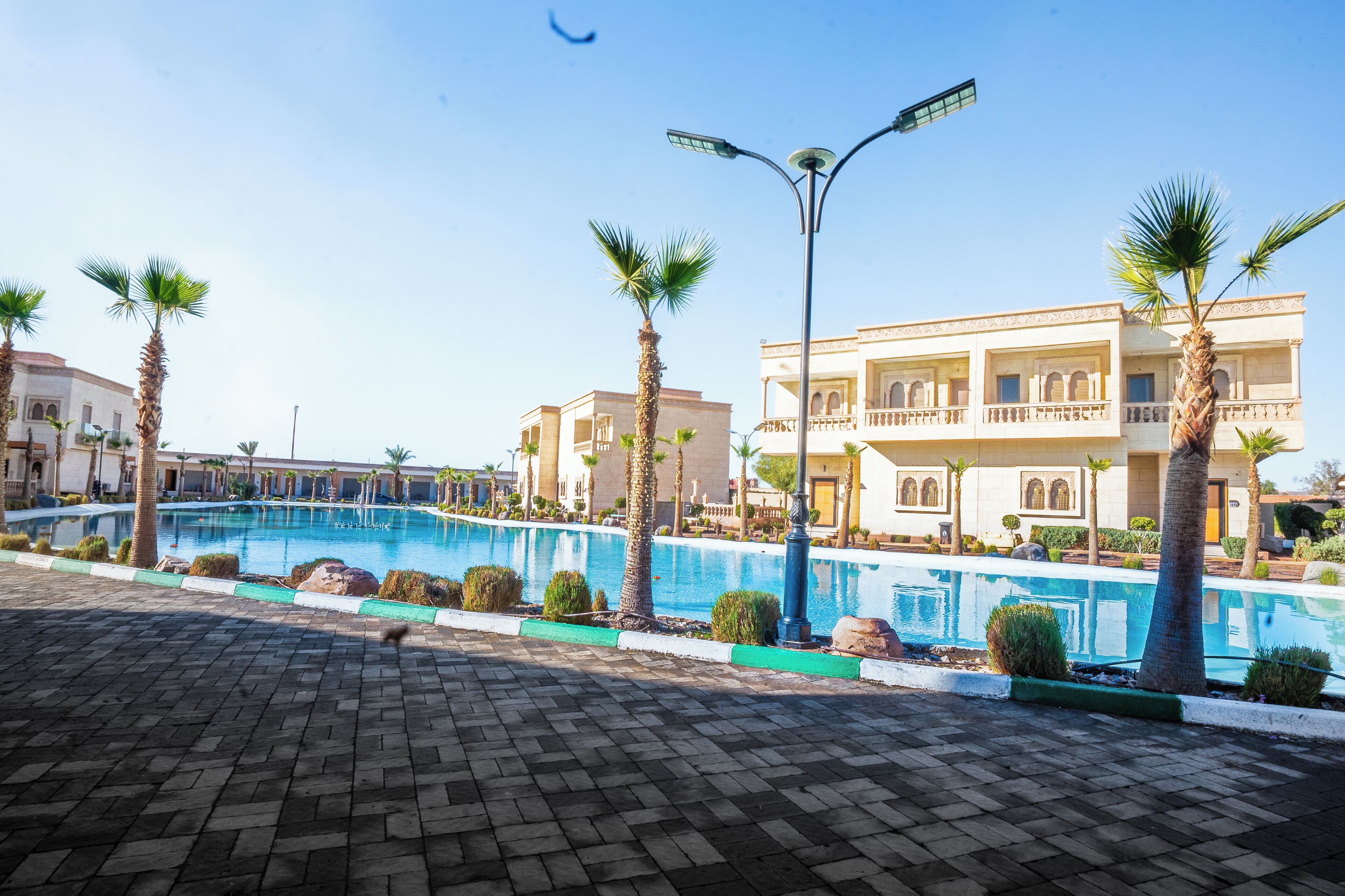Una piscina con un pavimento, palmeras y un edificio con balcón.