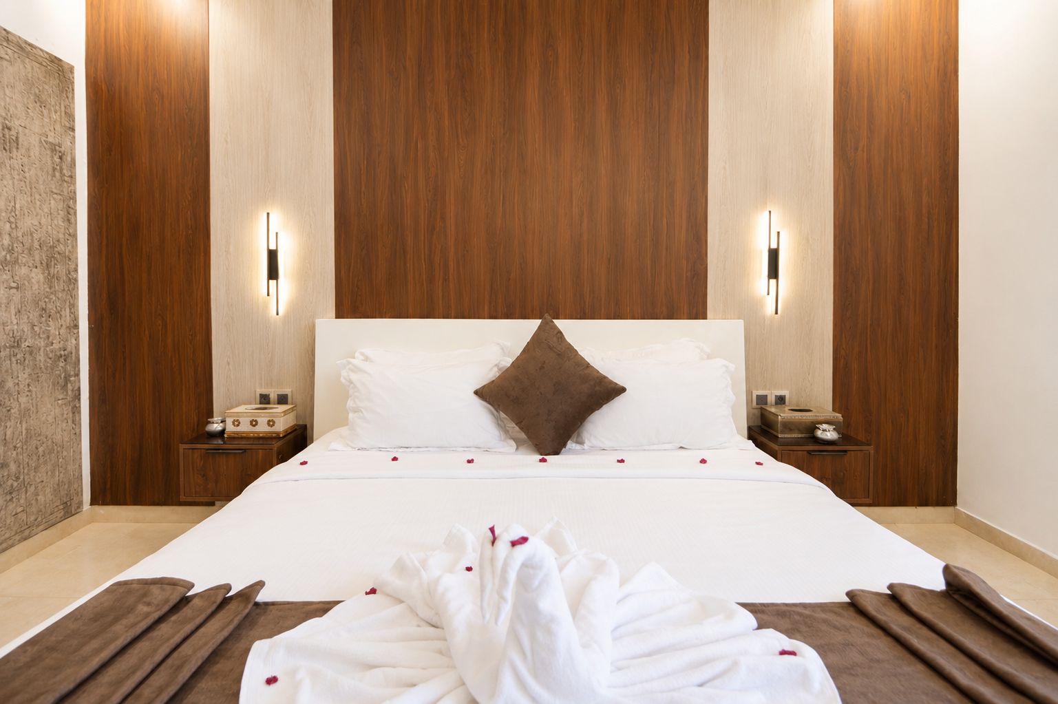 Una habitación de hotel con una cama grande, paneles de madera en las paredes, mesitas de noche con lámparas y una alfombra decorativa.