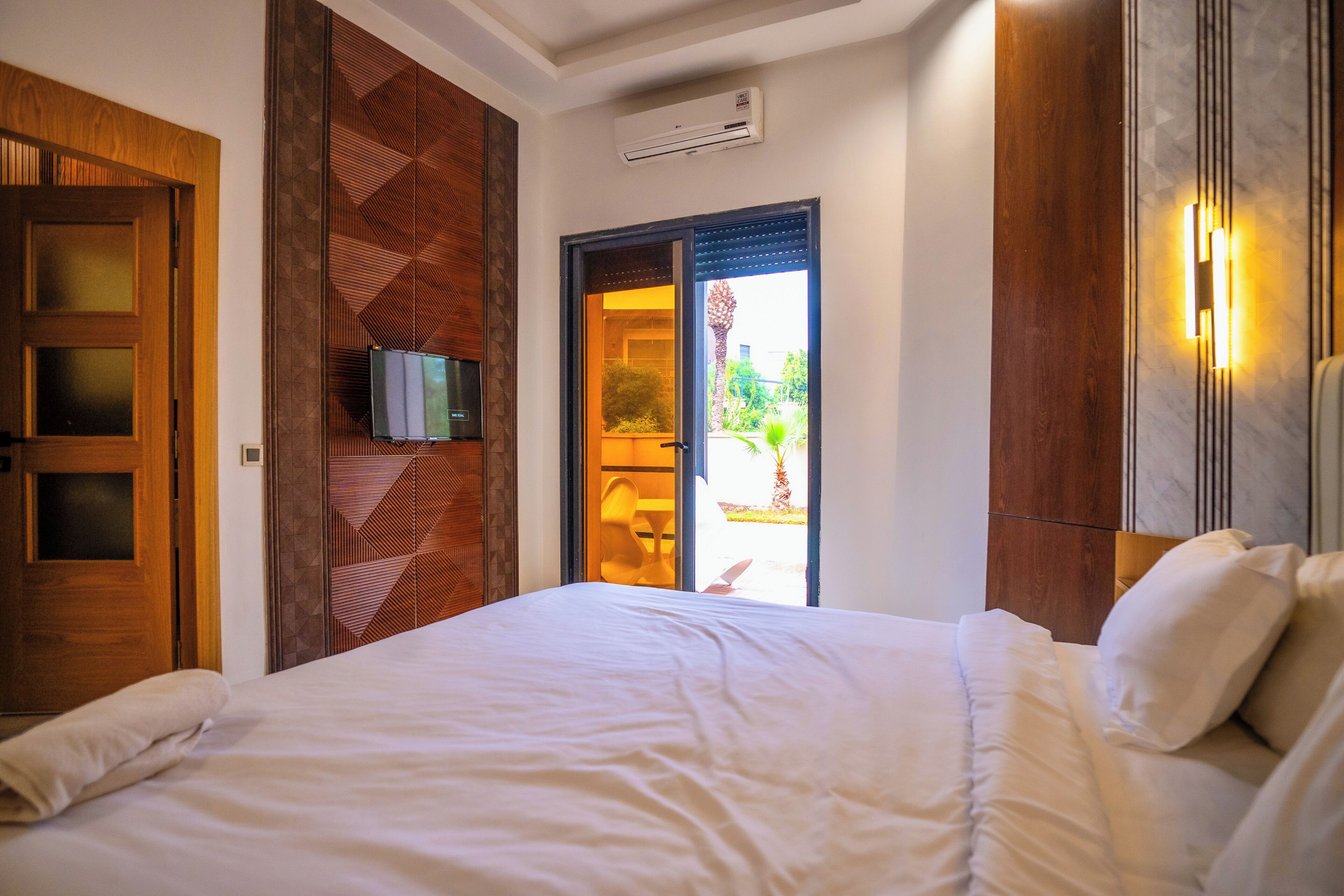 A hotel room with a bed, a television, a sliding door to the balcony, and a wall-mounted air conditioning unit.