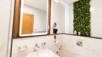 Un baño moderno con un lavabo de mármol, un espejo con marco de madera, un secador de pelo y un adorno verde en la pared.