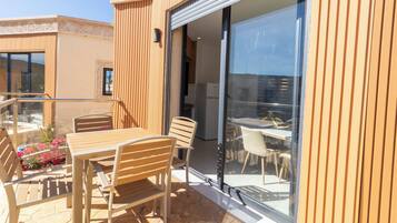 Une terrasse extérieure avec une table et des chaises en bois, une porte vitrée donnant sur un coin repas et un sol en pierre.