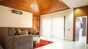 A modern living room with a wooden ceiling, a sofa with patterned cushions, a red rug, and a large window with sheer curtains. - rose garden resort marrakech (Marrakech)