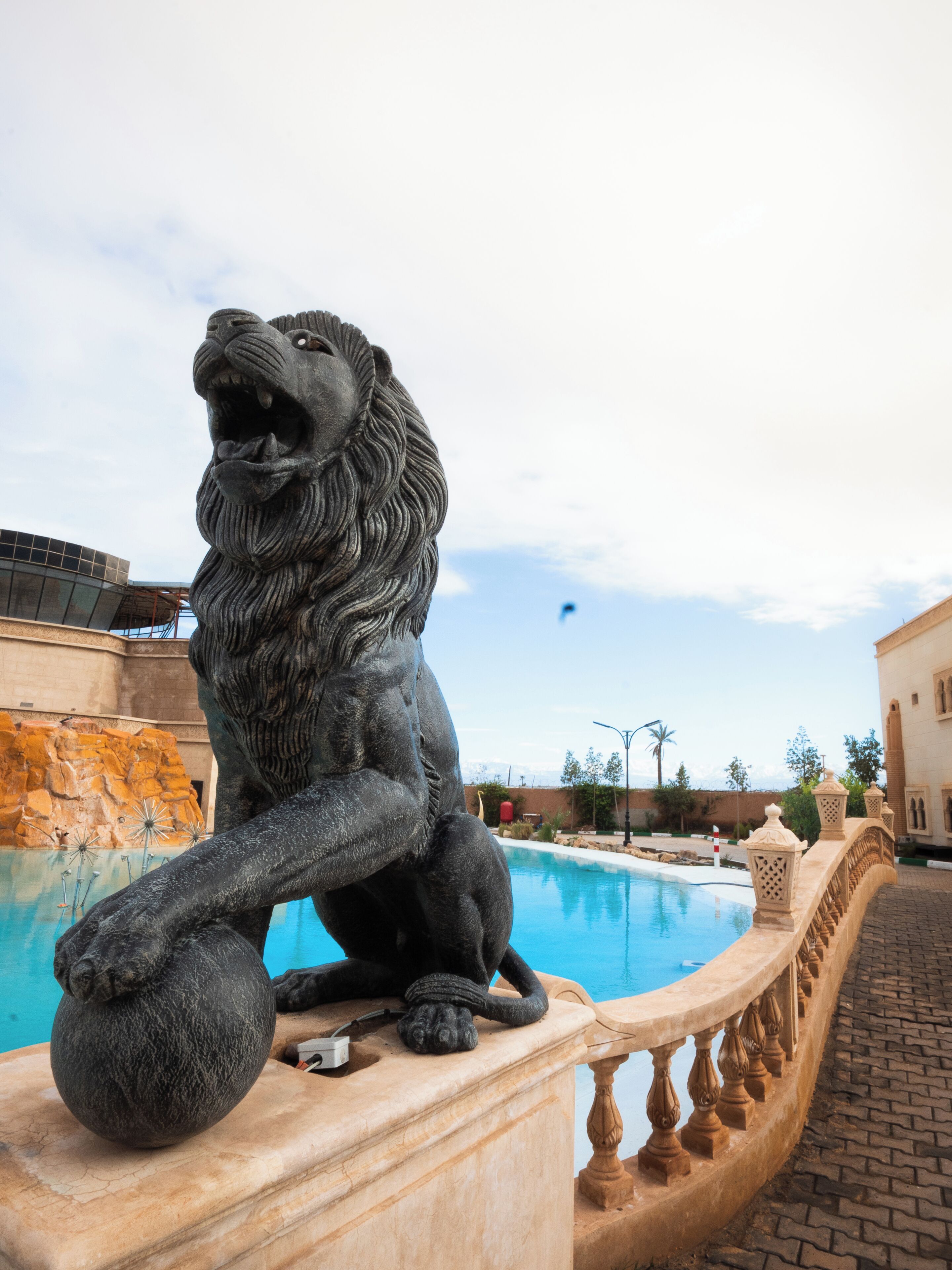Una estatua de león de piedra junto a una piscina, con vista despejada a la piscina y un edificio al fondo.