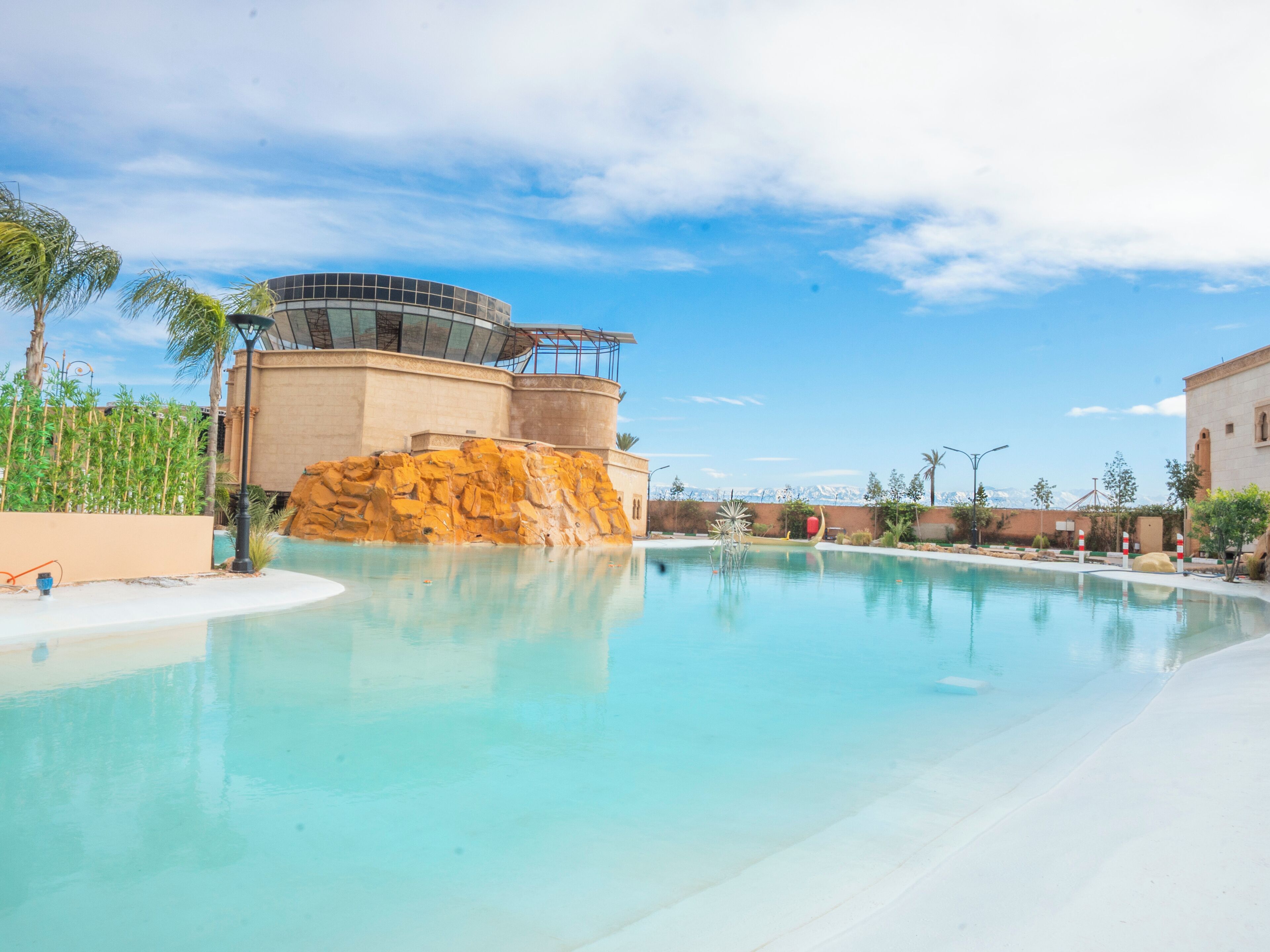 Piscina de resort com água cristalina, uma formação rochosa e um edifício moderno com fachada de vidro.