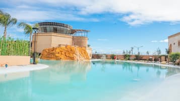 Piscina de resort com água cristalina, uma formação rochosa e um edifício moderno com fachada de vidro.