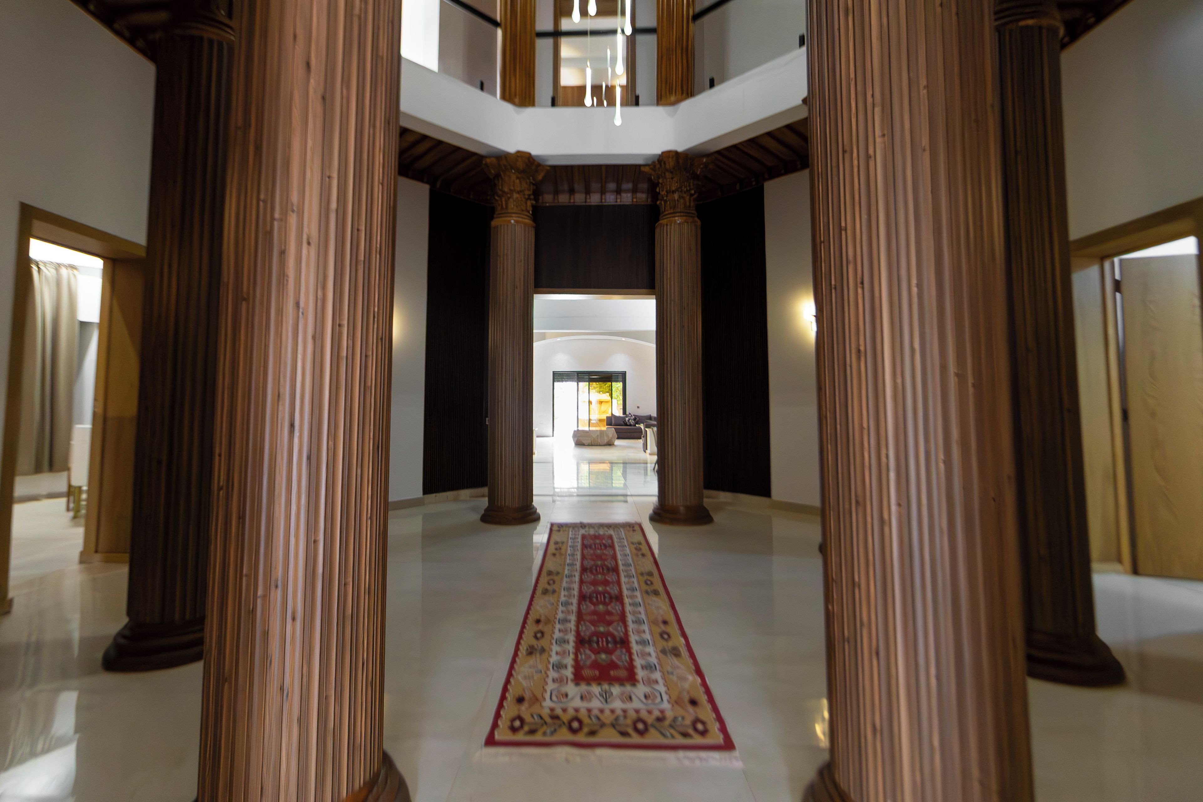 Un vestíbulo amplio con techos altos, grandes columnas de madera y un pasillo central con alfombra que conduce a una zona de estar.