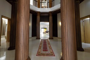 Un vestíbulo amplio con techos altos, grandes columnas de madera y un pasillo central con alfombra que conduce a una zona de estar.