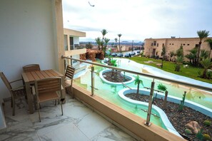 A balcony with a view of a landscaped pool area, including a rock formation and palm trees. - rose garden resort marrakech (Marrakech)