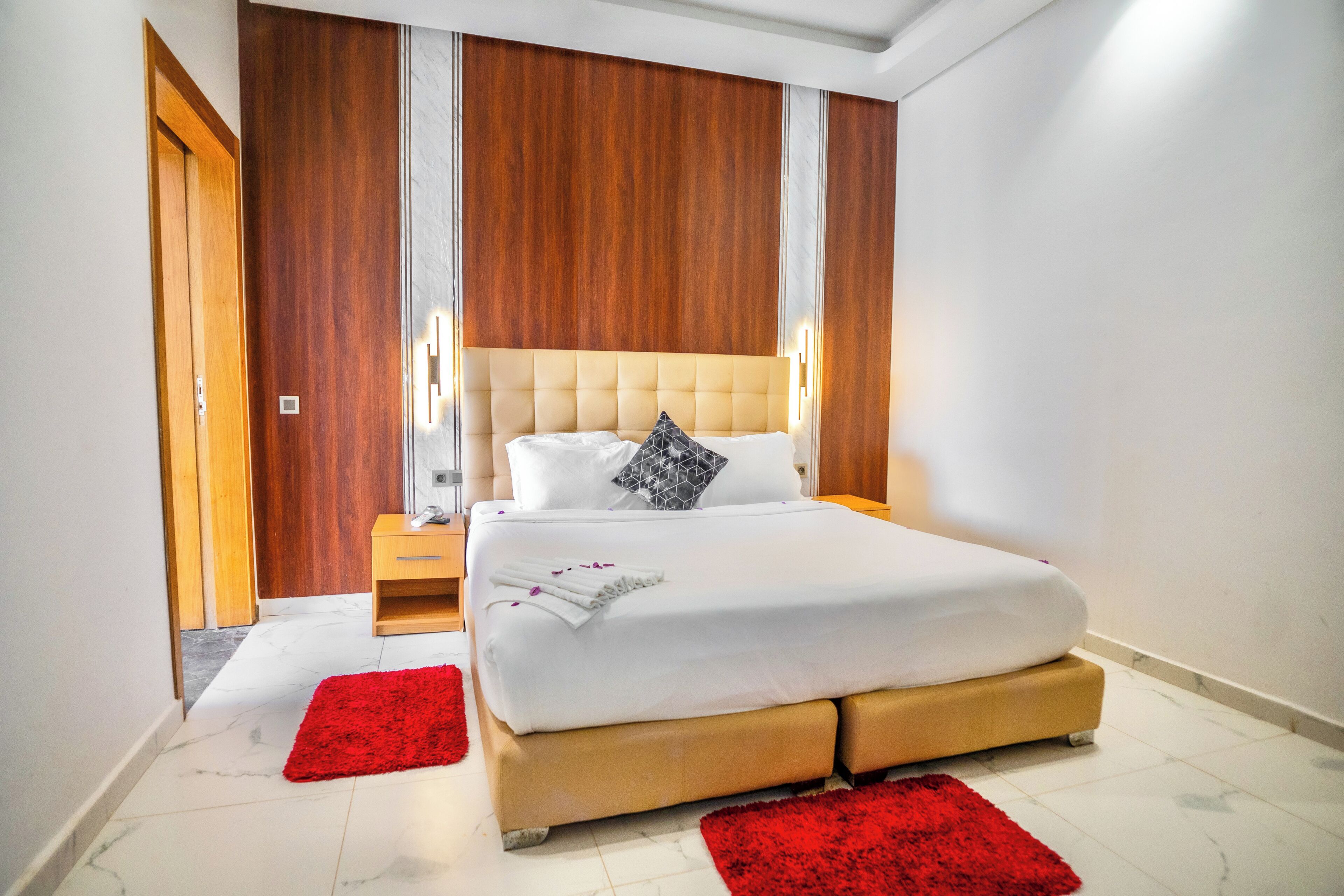 A hotel room with a large bed, wooden paneling on the walls, a nightstand, and a red rug.