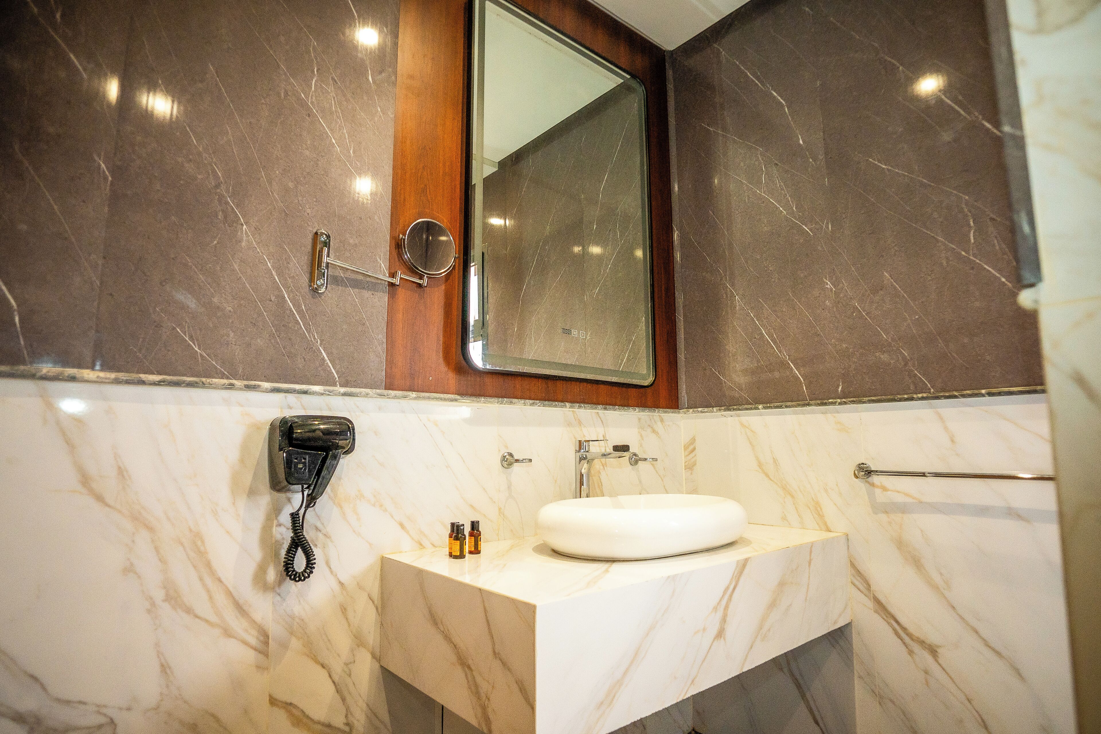 Un baño con lavamanos de mármol, espejo, secador de pelo y toallero.