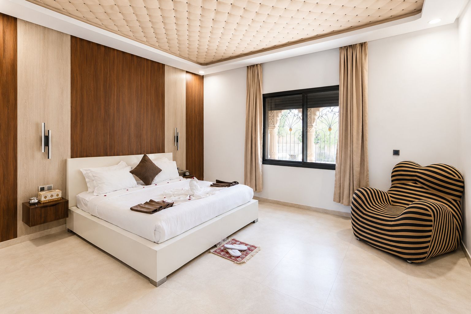Un dormitorio moderno con una cama grande, una mesita de noche, una ventana con cortinas y una silla a rayas.