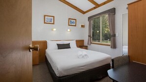 Ett hotellrum med en säng, sängbord, ett fönster med gardiner och väggmonterade lampor.