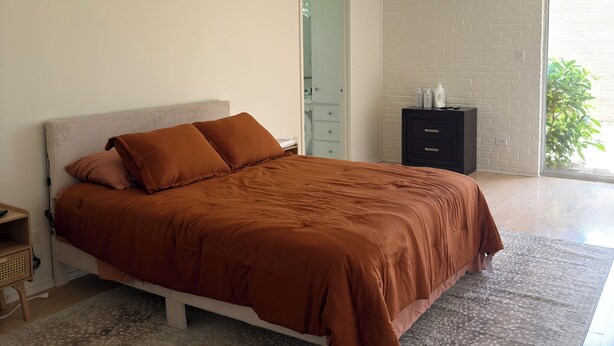 Une chambre à coucher avec un grand lit, une table de chevet, une commode et une fenêtre donnant sur un beau paysage.