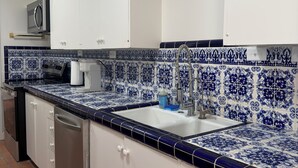 Une cuisine avec des meubles blancs, un crédence carrelée en bleu et blanc, un évier en acier inoxydable et un lave-vaisselle.